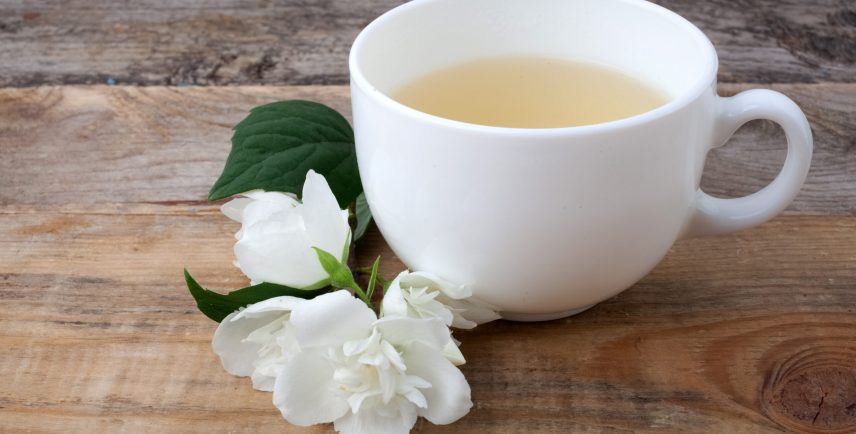 Glass cup of tea with jasmine flowers on dark wooden background.